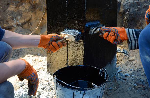 Builder worker painting black coal tar or bitumen at concrete surface by the brush. stock photo