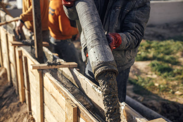 Builders pouring concrete with pump truck in wooden formwork with reinforcement. Workers pouring concrete in formwork for foundation. Construction site, process of house building stock photo