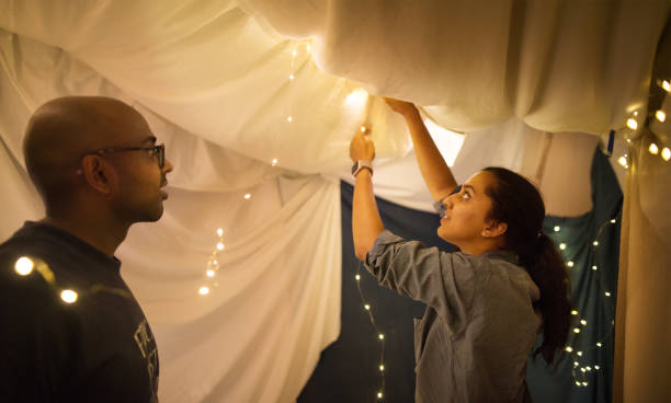 Building a blanket fort inside home Shot of a couple adding lights to a tent made in their living room fort stock pictures, royalty-free photos & images