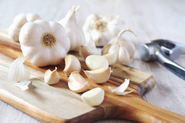 Bulbs of garlic on cutting board and garlic press stock photo