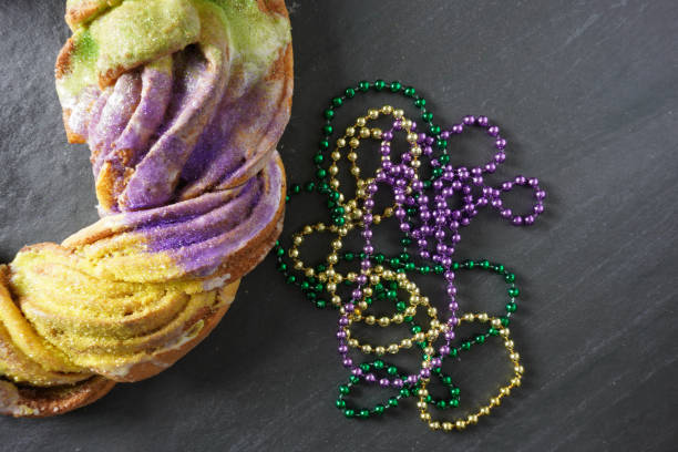 a bunch of green, gold and purple mardi gras beads next to a king cake on a gray slate background; copy space - carnival accessories flat lay imagens e fotografias de stock