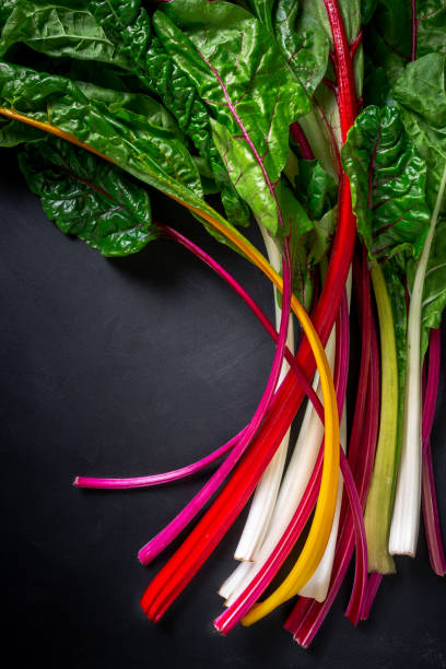 A bunch of rainbow chard on a black background, top down view Colorful rainbow chard on black table chard stock pictures, royalty-free photos & images