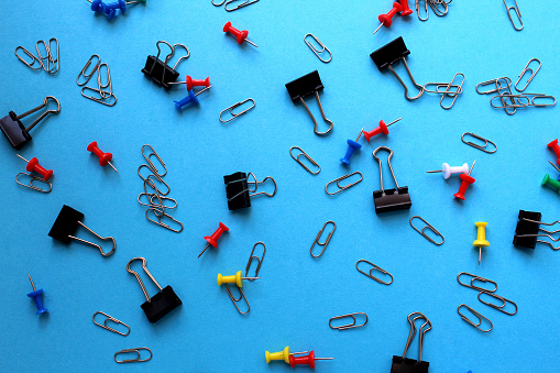 A bunch of stationery clips, pins and clothespins lie on a blue background.