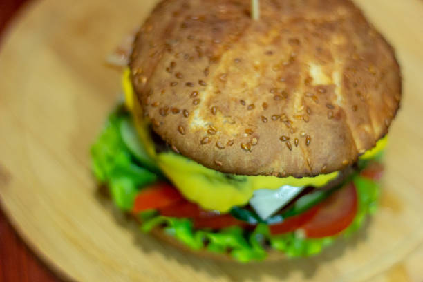 Burger from a meat patty with fresh cucumbers, tomatoes and cheese. White bun sprinkled with sesame seeds. Close-up stock photo
