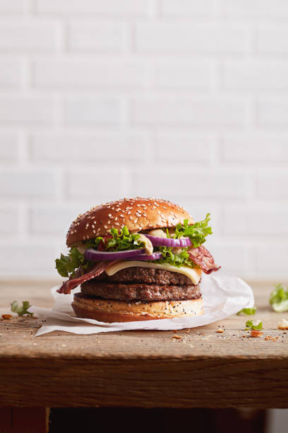 burger with sesame bun with onion rings and juicy fried meat on a white brick wall background, ready poster for print burger with sesame bun with onion rings and juicy fried meat on a white brick wall background juicy photos stock pictures, royalty-free photos & images