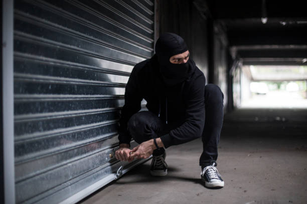 Burglar breaking into a garage Burglar trying to rob a garage. Unrecognizable Caucasian male wearing a balaclava. ski mask criminal stock pictures, royalty-free photos & images