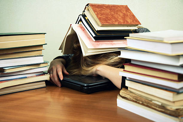 Buried in books young woman sleeping on a laptop with a heap of books on her head buried stock pictures, royalty-free photos & images