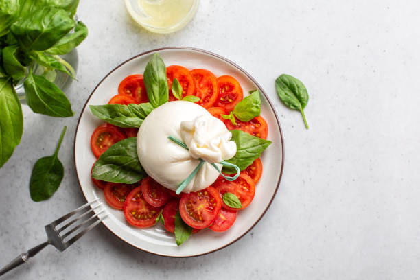 Burrata cheese with tomatoes and basil leaves. Caprese salad. Directly above, light table. stock photo