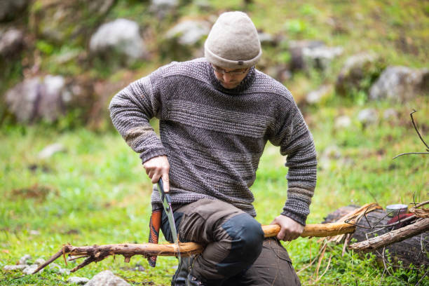 A bushcraft man sawing wood outdoors at camp An outdoors man in warm clothing demonstrating a safe way to saw wood for a camp fire outdoors. bushcraft stock pictures, royalty-free photos & images