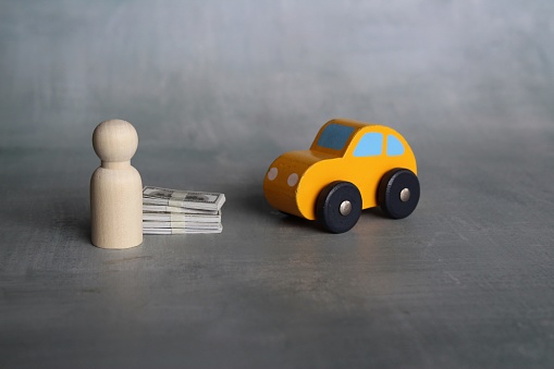 Business, car ownership and transportation concept. Wooden doll, stack of money and car.