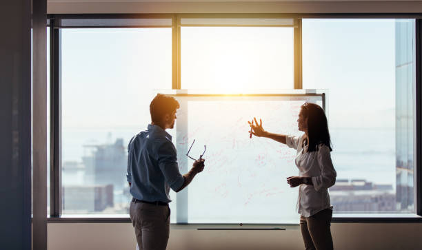 Business colleagues discussing ideas in office. Businesswoman making a presentation of ideas on whiteboard in boardroom. Two colleagues discussing business ideas in office. whiteboard visual aid stock pictures, royalty-free photos & images