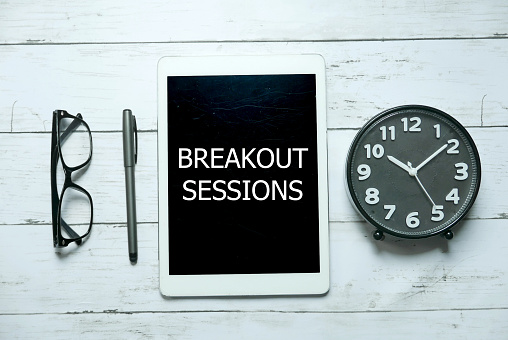 Business concept. Top view of glasses,pen,clock and tablet written with Breakout Sessions on white wooden background.