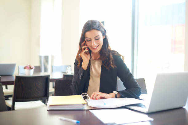 Business consultant Shot of a young businesswoman sitting at office desk in front of laptop and making call while considering the possibilities with her client. assistant stock pictures, royalty-free photos & images