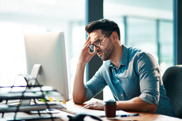 Business is putting him in a bad mood Shot of a young businessman looking displeased while using a computer at his work desk i don't know  stock pictures, royalty-free photos & images