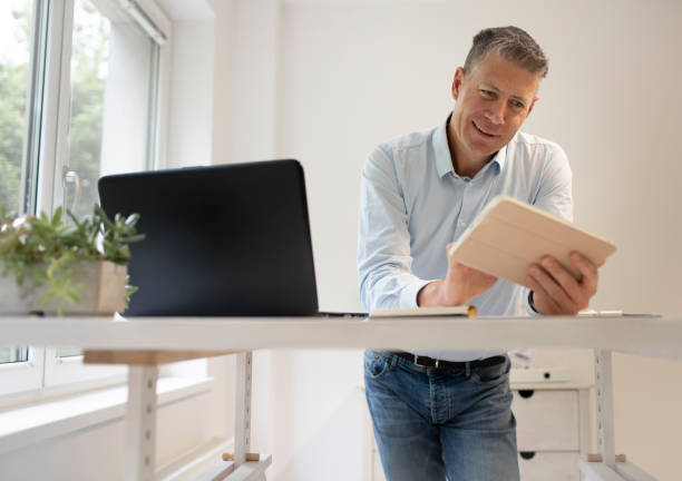 business man is standing behind high standing table and is working with his tablet stock photo