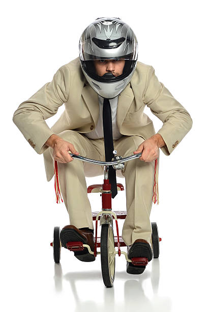 Business Man on Tricycle Business man with helmet riding child's tricycle isolated over white adult tricycle stock pictures, royalty-free photos & images