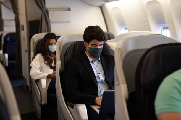 Business man traveling and wearing a facemask on the plane Business man traveling and wearing a facemask on the plane while using his laptopâ COVID-19 pandemic lifestyle concepts passenger stock pictures, royalty-free photos & images