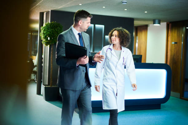 business medical meeting a businessman chats with a female doctor as they leave a boardroom meeting in a hospital administrator stock pictures, royalty-free photos & images