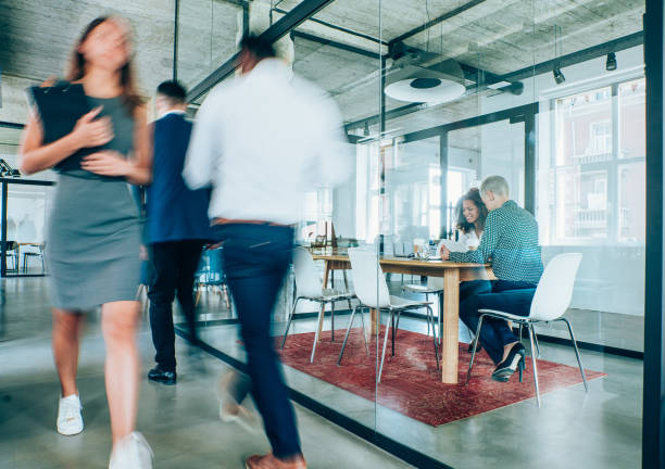 Business meeting at busy corporate office. Young entrepreneur having a business meeting inside of an office while their colleagues are walking in blurred motion. busy office stock pictures, royalty-free photos & images
