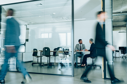 Shot of businesspeople having a business meeting inside of an office while their colleagues are walking in blurred motion.