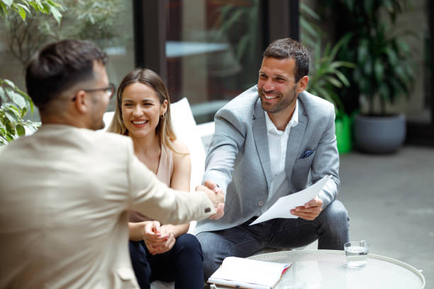 Business meeting Shot of three people with smiley faces at the meeting in the foyer of the company's building. Two businessmen are shaking hands after successfully concluding the business. georgijevic coworking stock pictures, royalty-free photos & images