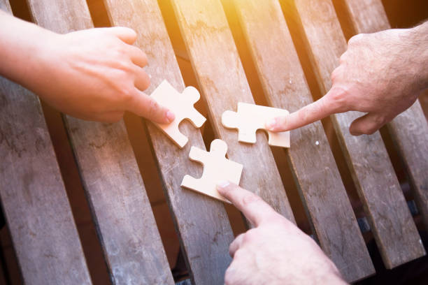 Business partnership or teamwork concept Business partnership or teamwork concept with a business people presenting a matching puzzle piece as they cooperate on finding an answer and solution, close up of their hands. coalition stock pictures, royalty-free photos & images