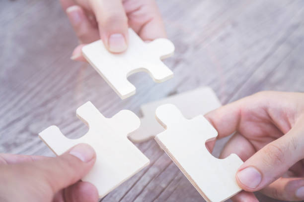 Business partnership or teamwork concept with a business people presenting a matching puzzle piece as they cooperate on finding an answer and solution, close up of their hands. stock photo