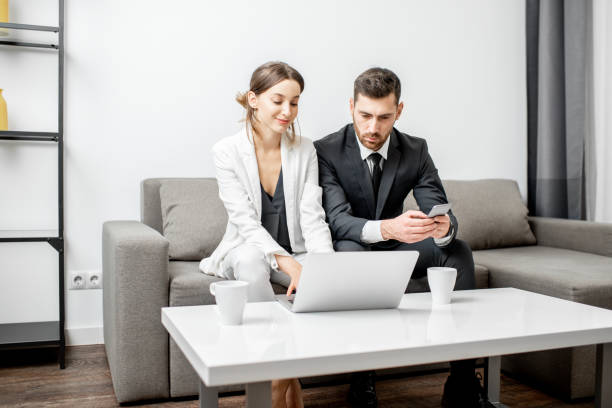 Business people on the couch at home Elegant businessman and woman sitting together on the couch during the work with laptop at home or comfortable office Mortgage Refinancing stock pictures, royalty-free photos & images