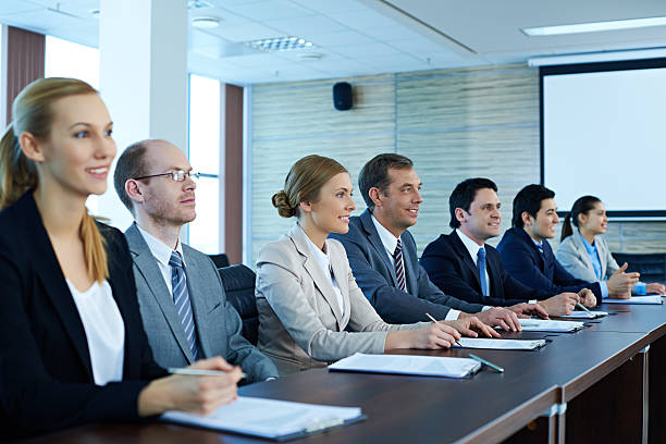 Business people sitting in a row at conference table Business people sitting in a row at conference table and listening to presentation shareholder stock pictures, royalty-free photos & images