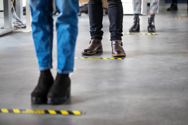 uomini d'affari in piedi dietro la segnaletica di distanziamento sociale sul pavimento dell'ufficio - concetti e temi foto e immagini stock