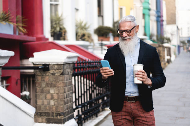 Business senior man using mobile phone and drinking coffee with city in background - Business senior man using mobile phone and drinking coffee with city in background - baby boomers stock pictures, royalty-free photos & images