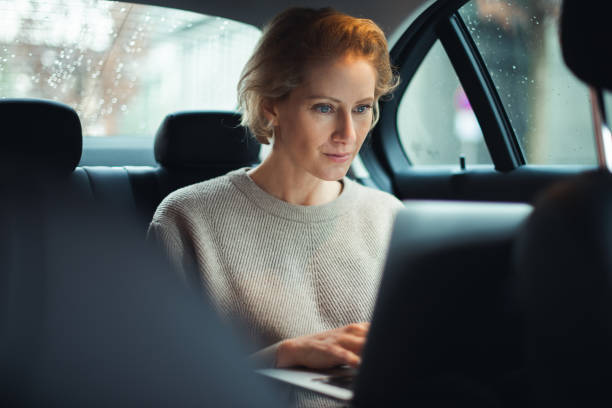 Business travel 40-year old business woman is traveling by car. She is sitting on the back seat and working on the laptop. georgijevic frankfurt stock pictures, royalty-free photos & images