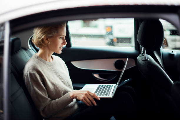 Business travel 40-year old business woman is traveling by car. She is sitting on the back seat and working on the laptop. georgijevic frankfurt stock pictures, royalty-free photos & images