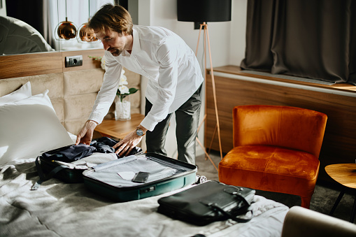 Businessman standing above bed in the hotel room packing his Suitcase for a Trip, Travel Concept