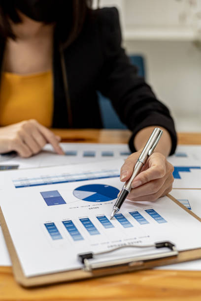 Business Woman holding a pen pointing to a bar graph document of company financial data, she is reviewing the company's monthly financial documents. Finance concepts and money management. stock photo