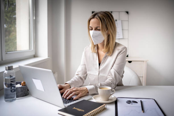 Business woman wearing ffp2 mask working on laptop in office stock photo