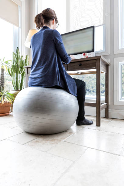 Business Woman Working from Home A business woman is managing her business from her home. She is sitting on a fitness ball to stay in shape. yoga ball work stock pictures, royalty-free photos & images