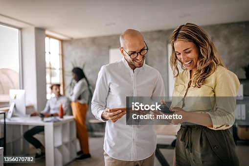 istock Businessman and businesswoman smiling looking at phone 1356070782