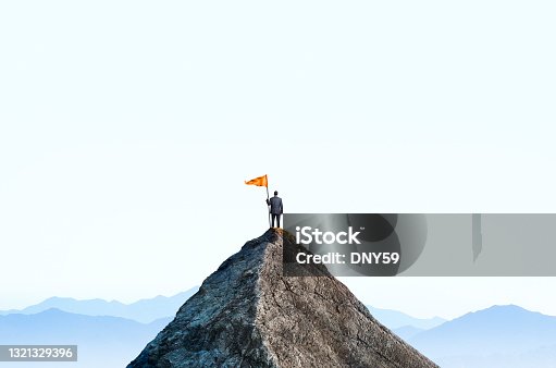 istock Businessman At Top Of Mountain Peak Holds Large Flag 1321329396