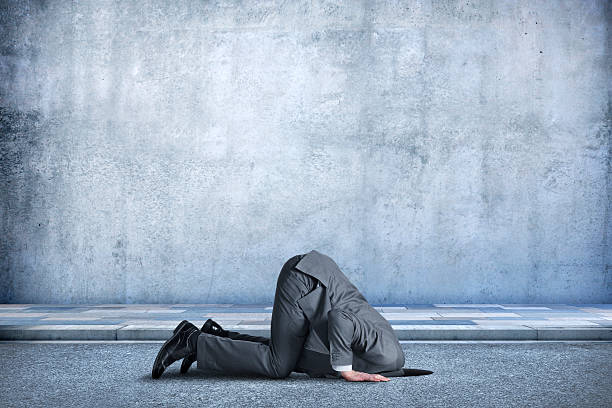 Businessman Bent Over With His Head In A Hole A businessman is bent over in the middle of the street as he buries his head in a hole in the ground.  The concrete wall behind him provides ample room for copy and text. ignorance stock pictures, royalty-free photos & images