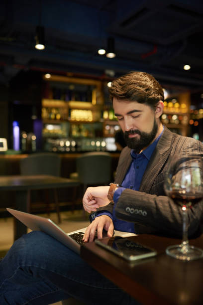 Businessman checking time Businessman checking time when working on laptop in bar at night bar drink establishment photos stock pictures, royalty-free photos & images