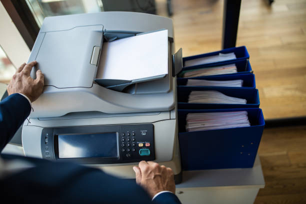 Businessman copying paper document on photocopier machine in office High angle view of unrecognizable businessman copying paper document on photocopier machine in office computer printer stock pictures, royalty-free photos & images