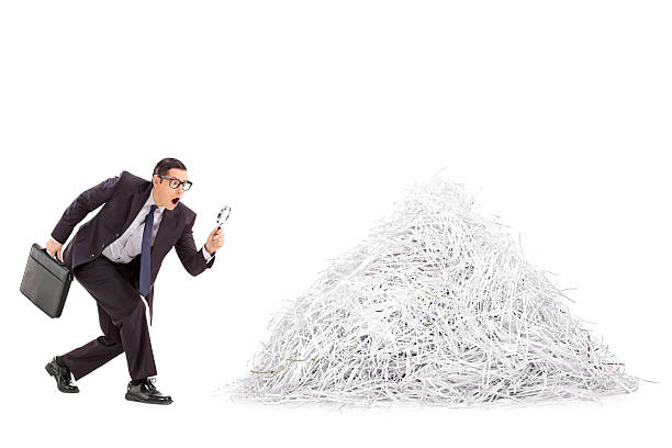 Businessman examining a pile of shredded paper Businessman examining a pile of shredded paper through a magnifying glass isolated on white background broken suitcase stock pictures, royalty-free photos & images