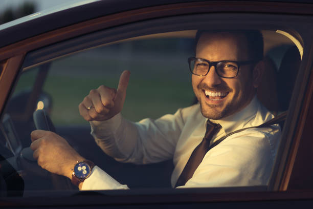 Businessman gesturing thumbs up while sitting in car stock photo