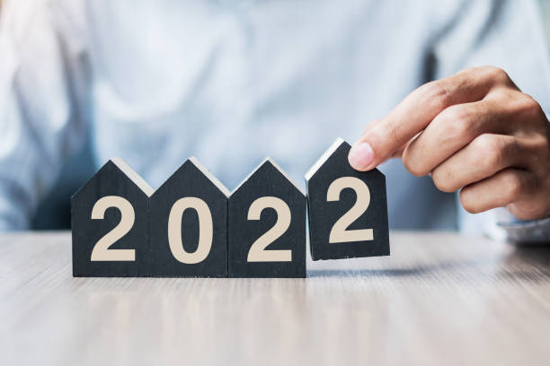 Businessman hands holding 2022 Happy New Year with house model on table office. New House, Financial, Property insurance, real estate, savings and New Year Resolution concepts stock photo
