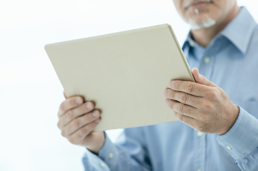 Businessman holding a tablet-pc in his hands in a close up cropped view on the digital notepad over a high key white background