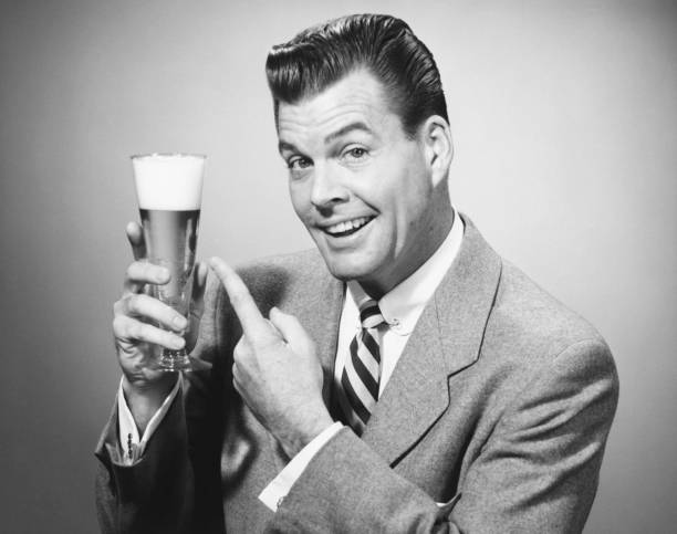 businessman in full suit in studio pointing at glass of beer, (b&w), portrait - ดื่มฉลอง ภาพถ่าย ภาพสต็อก ภาพถ่ายและรูปภาพปลอดค่าลิขสิทธิ์