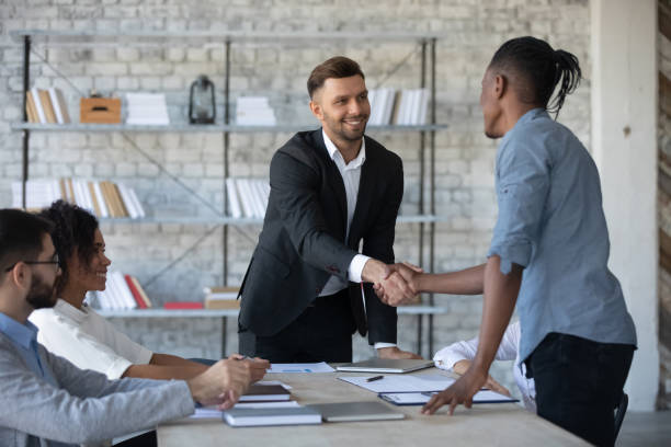 Businessman in suit shaking hand of african american male partner. Successful businessman in suit shaking hand of african american male business partner at company meeting. Diverse team fasten deal with applicant at hire. Leader with assistant congratulates clients. selling stock pictures, royalty-free photos & images