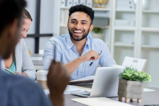 Businessman laughs while meeting with colleagues Handsome Indian businessman laughs while meeting with clients or colleagues. They are reviewing documents together. indian ethnicity photos stock pictures, royalty-free photos & images