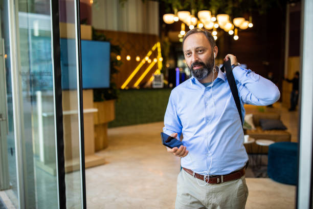 Businessman leaving office building after long day at work Mature bearded Man with headphones and shoulder bag leaving the business building after work after work stock pictures, royalty-free photos & images
